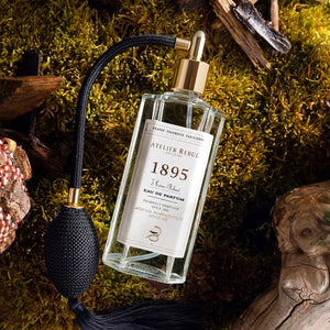 1895 parfum van Atelier Rebul in een glazen fles met textiel verstuiver. De parfum ligt op groen mos met hout aan de randen.