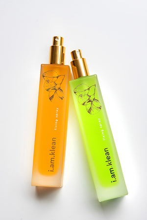 Fixerende sprays van i.am.klean in het oranje en groen. De oranje fixing spray heeft een glanzend effect voor droge huid, de groene een matterend effect voor vette huid. De foto heeft een witte achtergrond.
