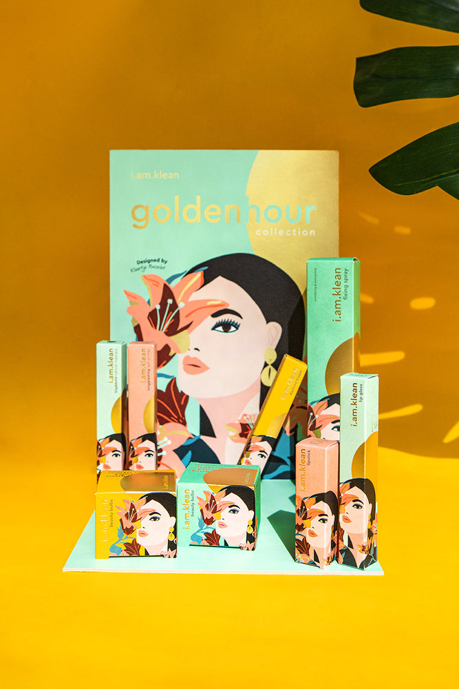 Golden hour collectie van i.am.klean met de display en de minerale make-up van de nieuwe collectie. De display heeft een blauwe en gouden kleur met de tekening van een vrouw met een bloem. De foto heeft een gouden achtergrond.